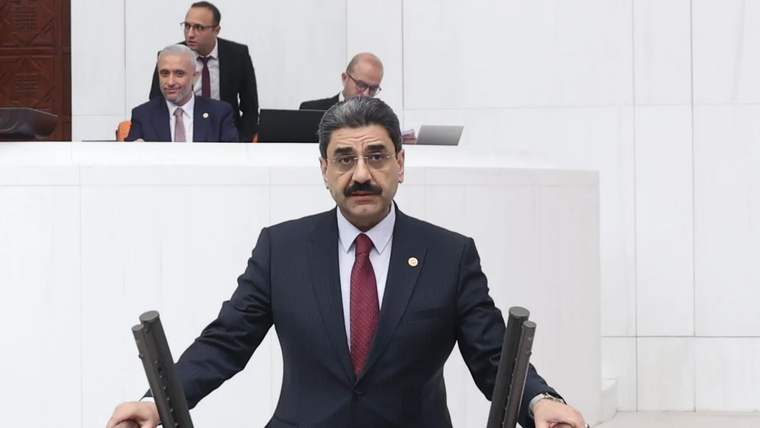 Kürsüde konuşan bir kişi, arka planda birkaç kişi bilgisayar kullanıyor.