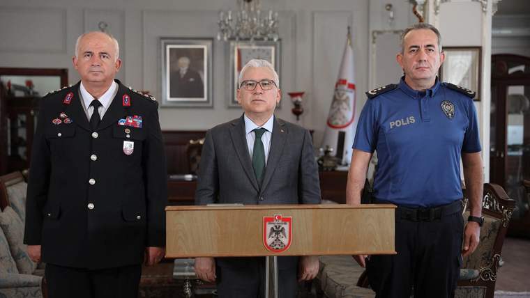 Kürsüde, iki polis memuru ve bir yetkili, arka planda Türk bayrağı ve Sivas tabelası ile duruyor.