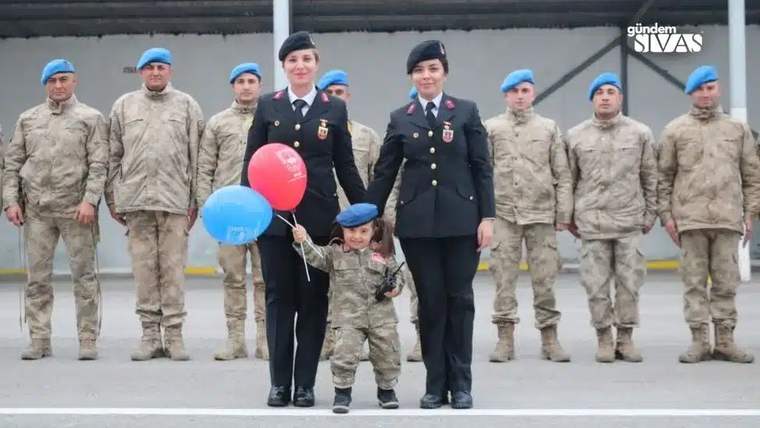 Askeri üniforma giymiş iki kadın, bir çocukla birlikte duruyor; çocuk balon tutuyor.