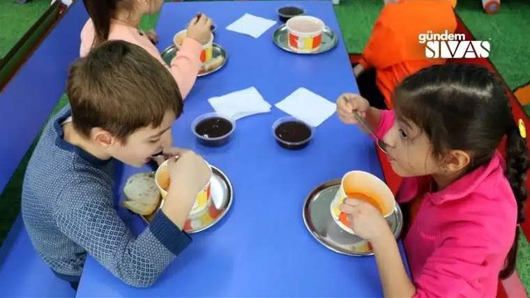 İki çocuk, masada çorba ve ekmek yerken, tabaklarından yemek yiyorlar.