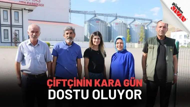 Fabrika binası ve siloların önünde duran beş yetişkin, kameraya doğru yan yana bakıyor.