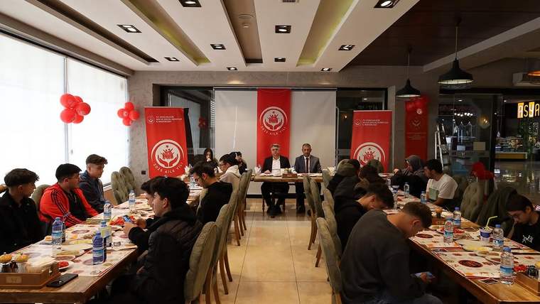 Restoran salonunda uzun masalarda oturan öğrenciler, karşılarındaki masada konuşan iki kişiyle birlikte görülüyor.