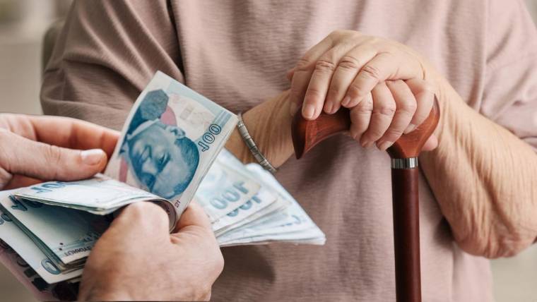 Bir kişinin elindeki Türk lirası banknotları, baston tutan kişinin önünde tutuluyor.