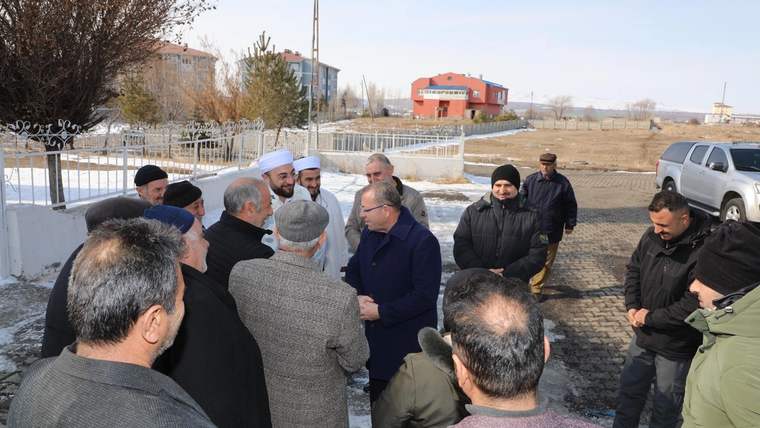 Karlı bir mahallede, kışlık giysili bir grup insan açık alanda sohbet ederken görülüyor.