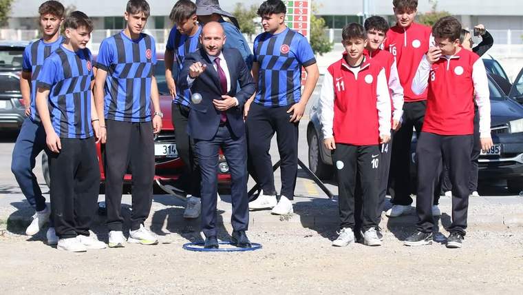 Bocce oynayan bir kişi, etrafında genç sporcular kalabalığı var.