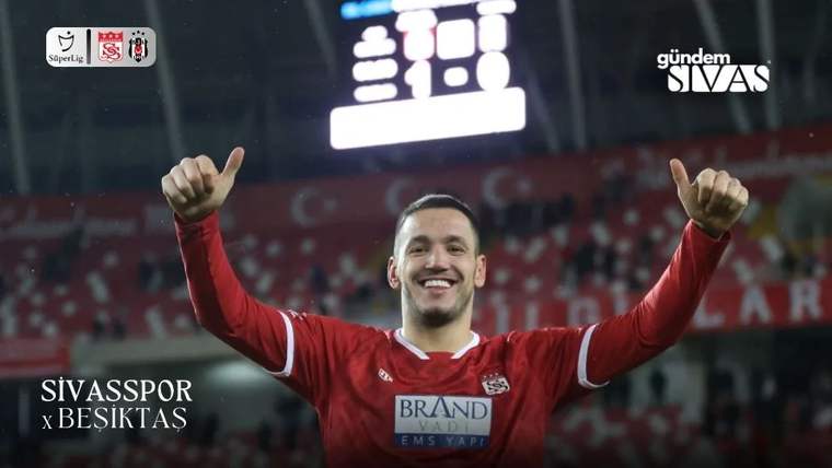 Kırmızı formalı bir futbolcu, stadyum tribünleri önünde iki başparmağını kaldırarak gülümsüyor.