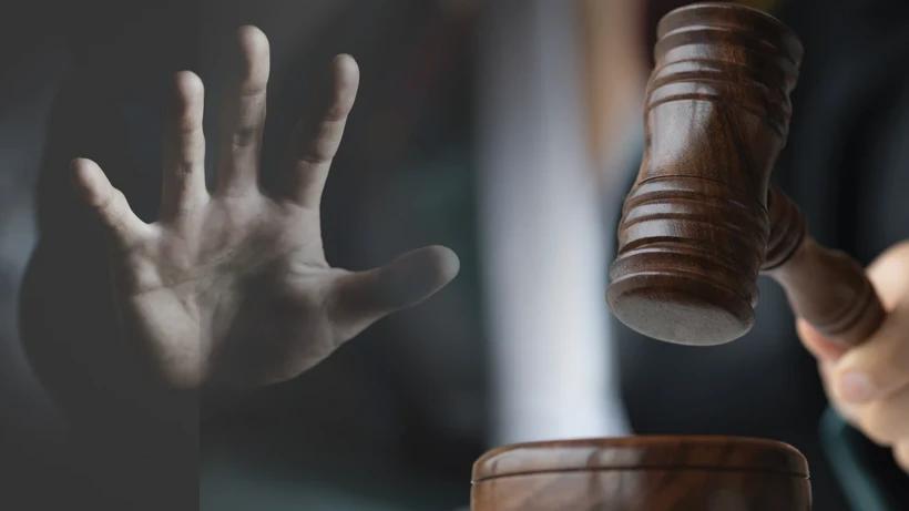 Koyu arka planda açık bir el ve yanında havada tutulan ahşap bir hâkim tokmağı görülüyor.