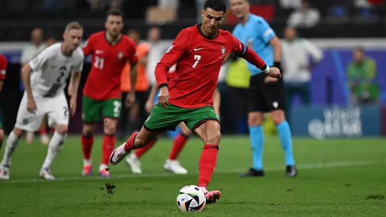 Kırmızı ve yeşil forma giymiş bir futbolcu, penaltı atışı yaparken topa vurmak üzere.