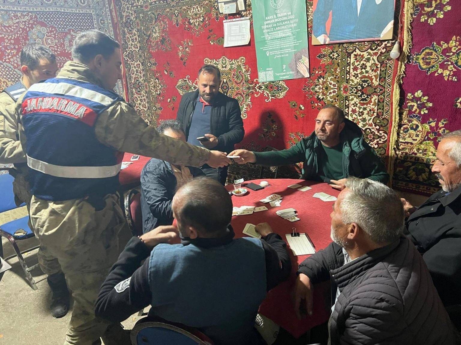 Jandarma yazılı yelek giyen bir görevli, halılarla süslü odada masadaki kişilerle el sıkışıyor.