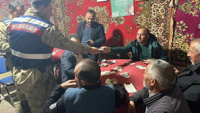 Jandarma yazılı yelek giyen bir görevli, halılarla süslü odada masadaki kişilerle el sıkışıyor.