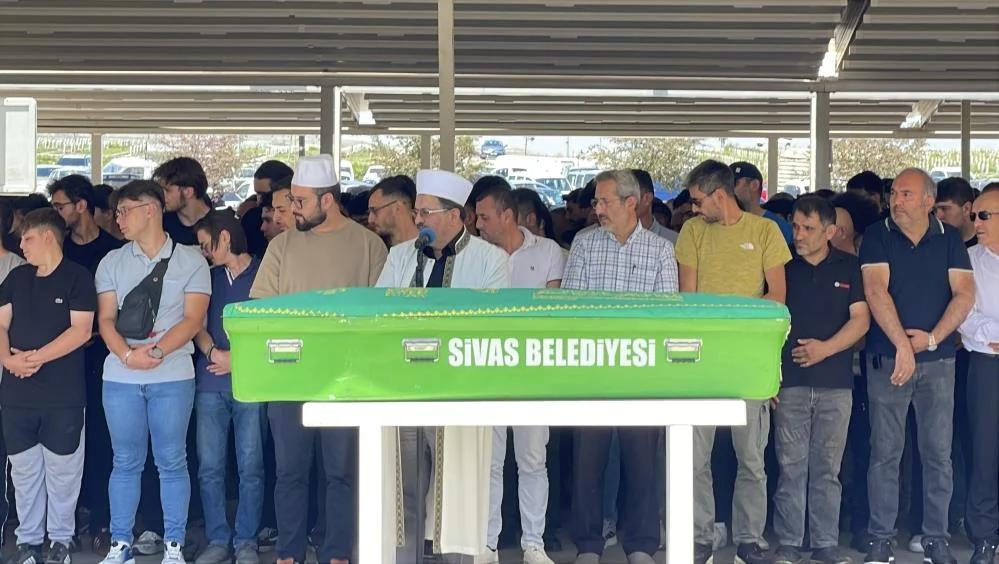 Yeşil bir tabutun önünde, kalabalık bir grup insan duruyor; bir kişi konuşma yapıyor.