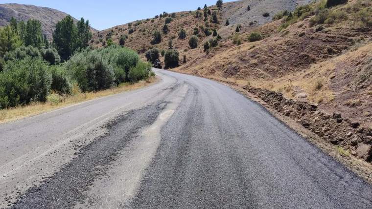 Hafik'te asfalt kaplama çalışması yapılan yol, çevresinde ağaçlar ve dağlık alanlar ile birlikte görünmekte.