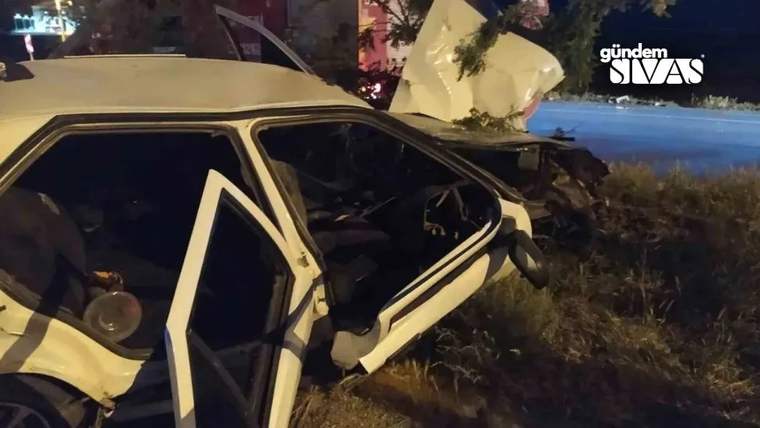 Gece yol kenarında duran beyaz otomobilin kapıları açık, ön kısmı ve gövdesi ağır hasarlı görünüyor.