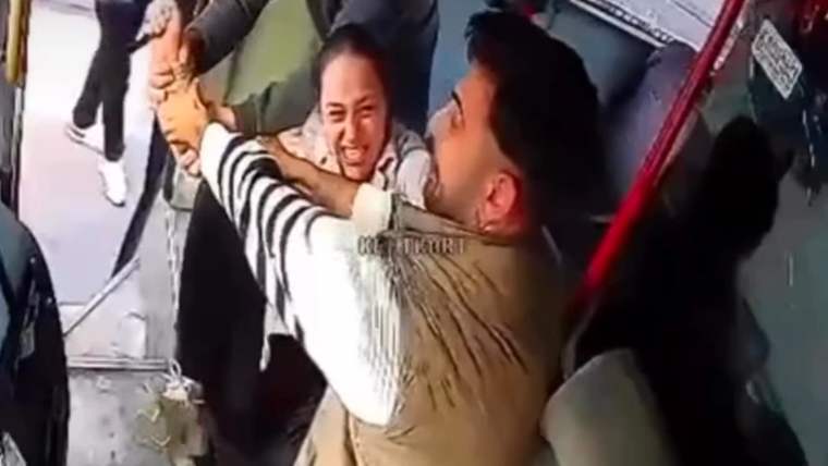 Otobüs içinde bir kadınla bir erkek karşılıklı dururken, başka bir kişi kadının kollarını tutuyor.