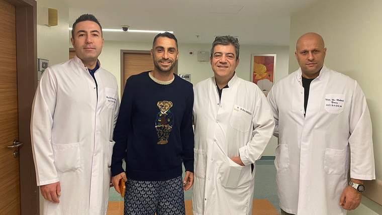 Bir koridorda üç beyaz önlüklü kişi ile spor giyimli bir adam yan yana duruyor.