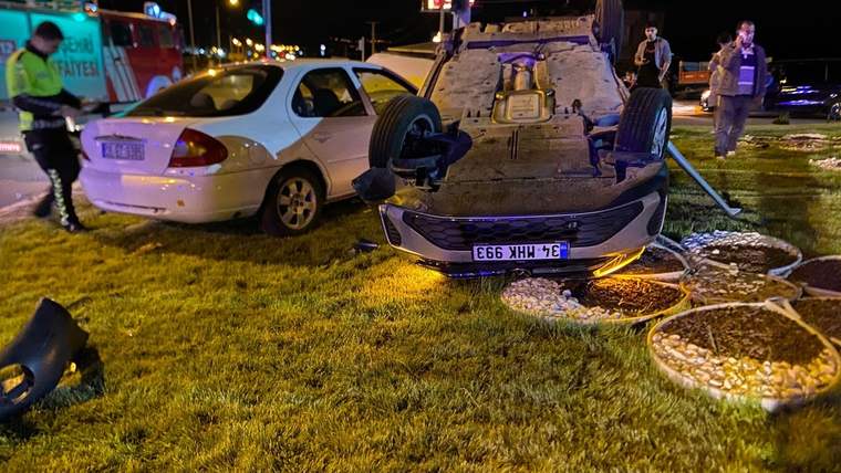 Gece yol kenarında ters dönmüş bir otomobil, yanında beyaz sedan ve çevrede inceleme yapan görevliler görülüyor.