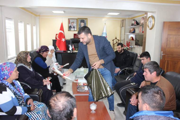 Bir odada oturan kalabalık arasındaki erkek, elindeki paketi karşısındaki kişiye uzatıyor.
