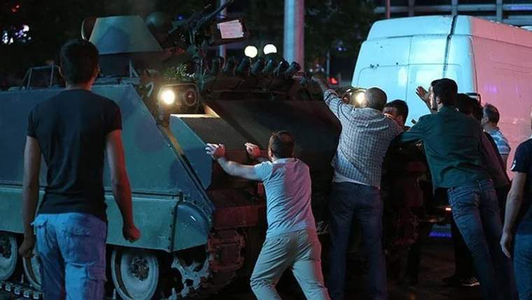 Bir grup insan, bir askeri aracı itmeye çalışıyor.