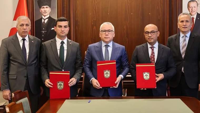 Bir grup insan, masada belgelerle birlikte poz veriyor. Arka planda Atatürk portresi var.