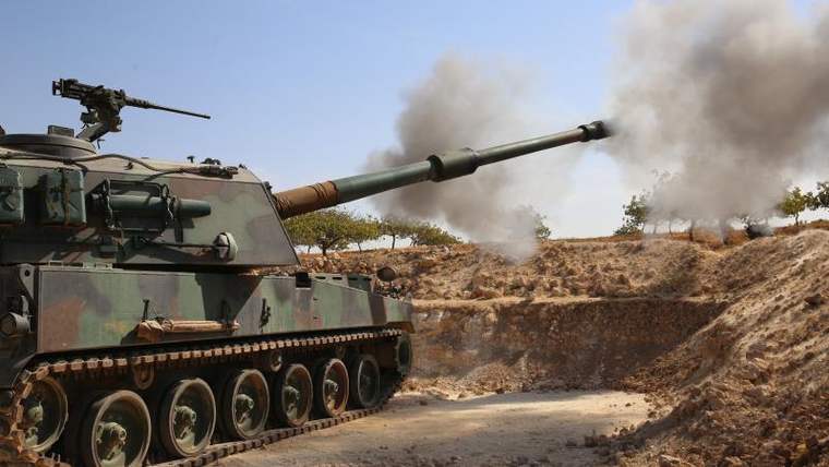 Bir tank, mermisini ateşleyerek duman çıkarıyor; arka planda ağaçlar var.