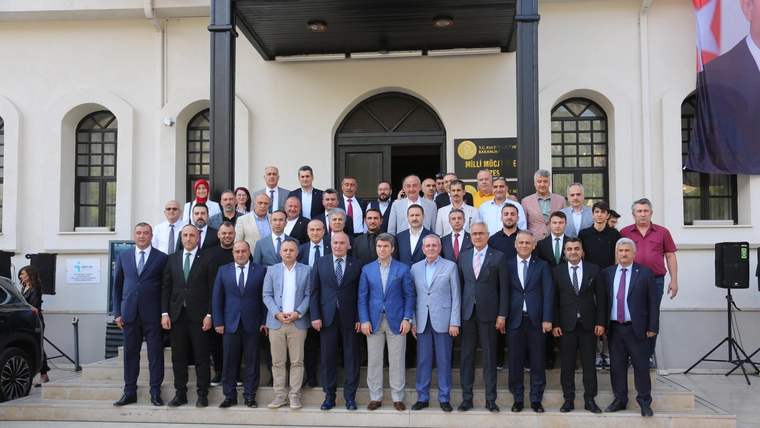 Bir binanın giriş merdivenlerinde, takım elbiseli ve günlük giyimli kalabalık bir grup birlikte duruyor.