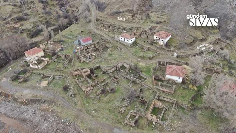Havadan görünümde, yamaçta harabe taş yapılar ve kırmızı çatılı birkaç evin bulunduğu terk edilmiş yerleşim