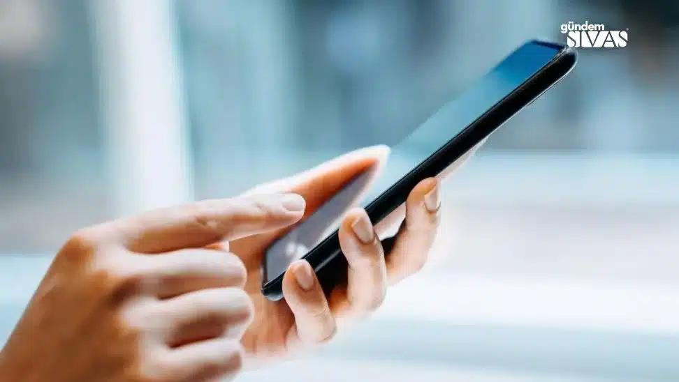 Bir elin tuttuğu akıllı telefonun ekranına diğer elin parmağıyla dokunuluyor.