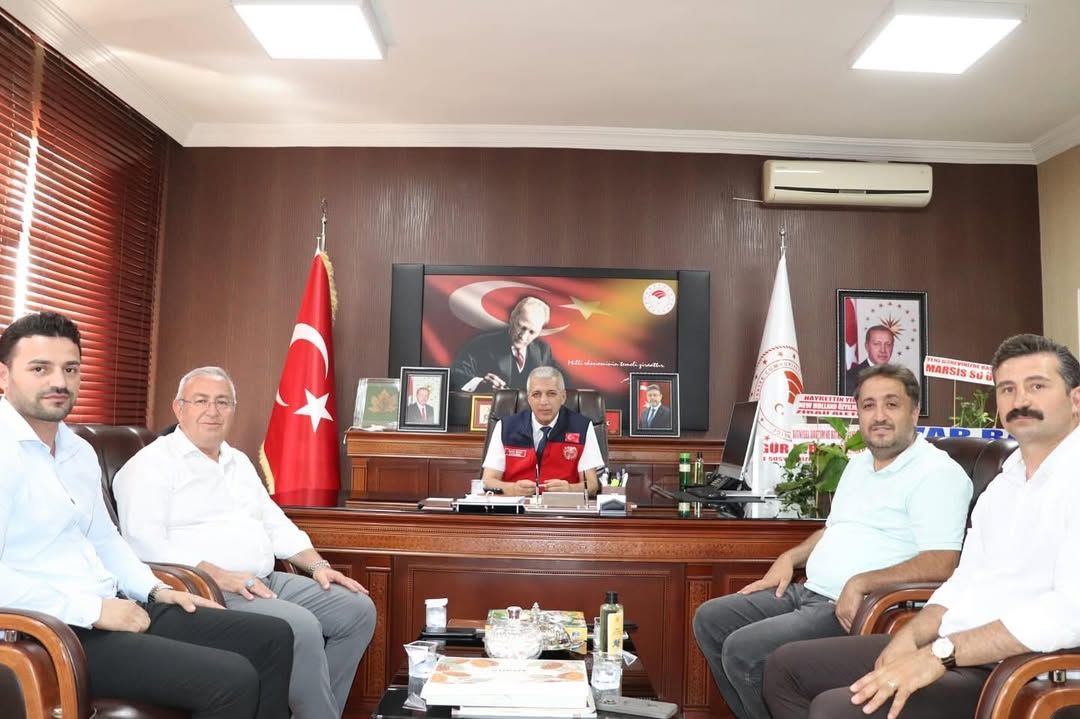 Bir masa etrafında oturan beş kişi, arka planda Türk bayrağı ve Atatürk posteri var.