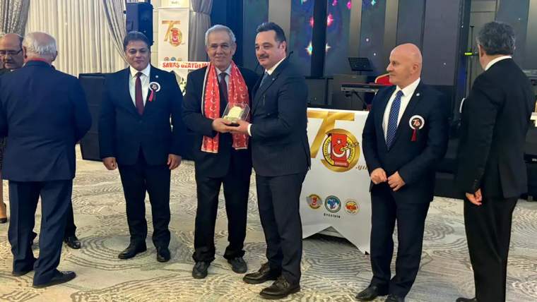 Dört kişi, bir plaketin verildiği tören sırasında sahnede duruyor.
