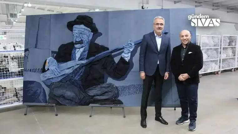 Sergi alanında, büyük mavi tonlu bir figür çalışmasının önünde duran iki kişi görülüyor.