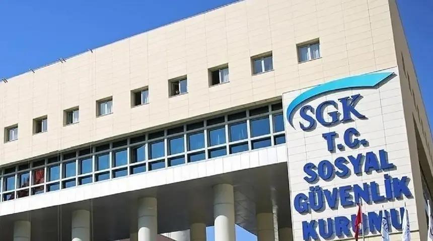 SGK ve T.C. Sosyal Güvenlik Kurumu yazılı tabelanın önünde, pencereli bir kamu binası görülüyor.