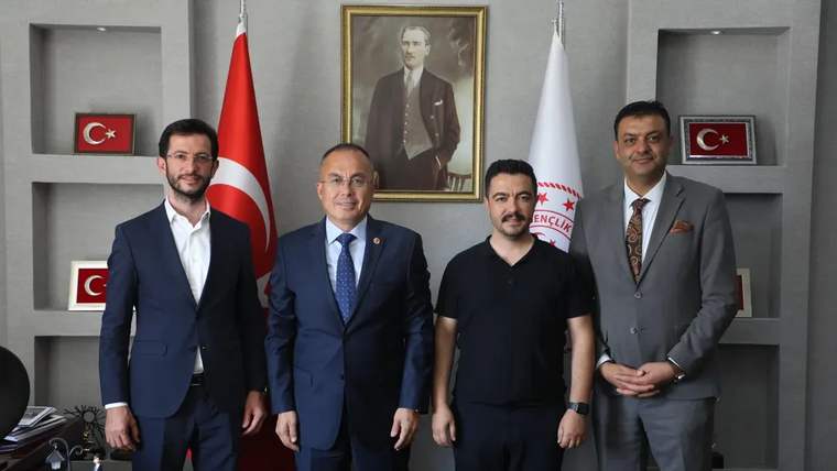 Sivas Gençlik ve Spor İl Müdürlüğü'nde dört kişi, masanın önünde duruyor. Arkada Atatürk'ün portresi ve Türk bayrağı var.