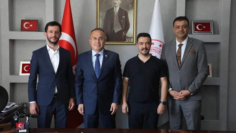 Sivas Gençlik ve Spor İl Müdürlüğü'nde dört kişi, masanın önünde duruyor. Arkada Atatürk'ün portresi ve Türk bayrağı var.