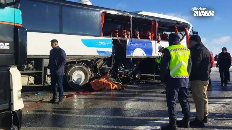 Hasarlı bir otobüsün çevresinde güvenlik yelekli kişiler duruyor; yol üzerinde kırılmış camlar ve parçalar görülüyor.