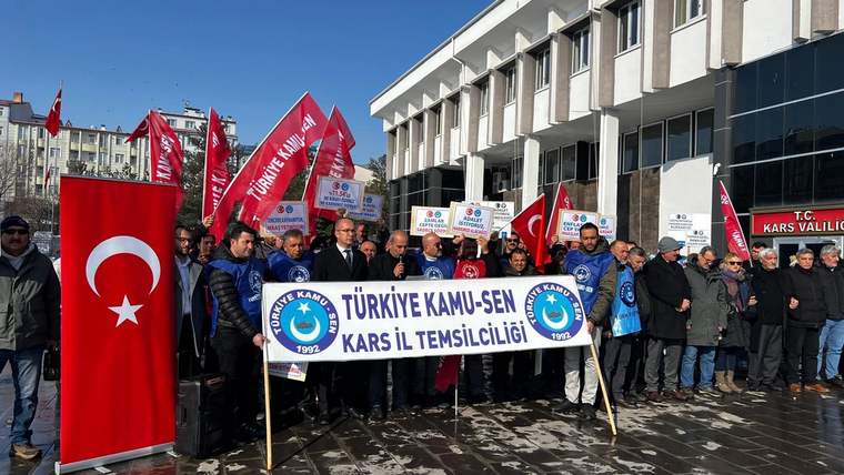 Türkiye Kamu-Sen Kars İl Temsilciliği pankartı taşıyan kalabalık, Türk bayraklarıyla bina önünde duruyor.