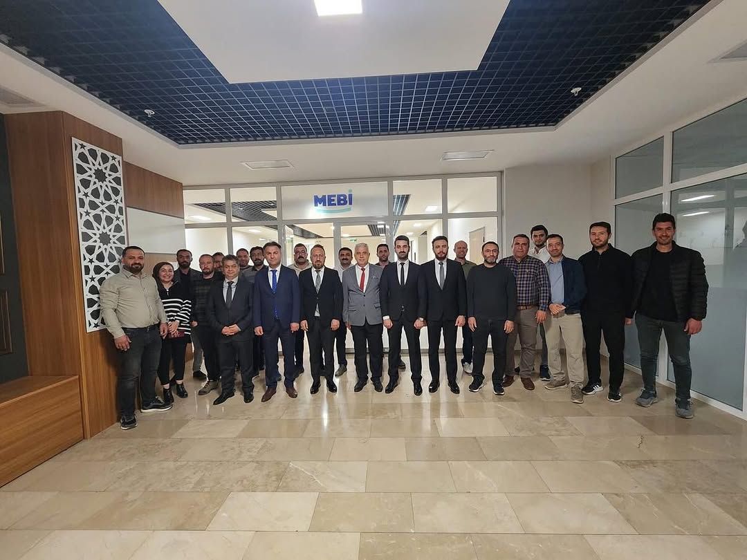 MEBİ yazılı bir alanın girişinde, koridorda yan yana duran kalabalık bir grup görülüyor.