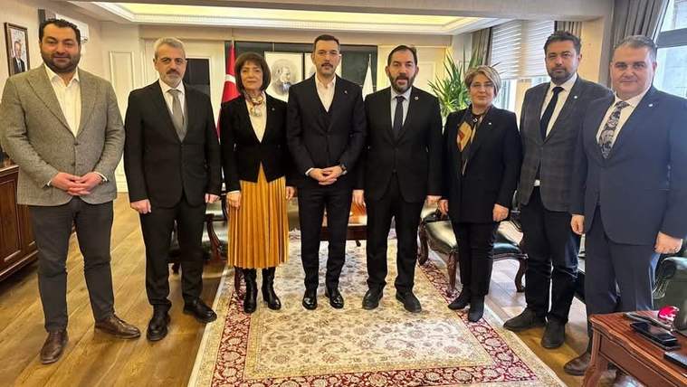 İç mekânda, takım elbiseli ve resmi giyimli yedi erkek ile iki kadın halı üzerinde yan yana duruyor.