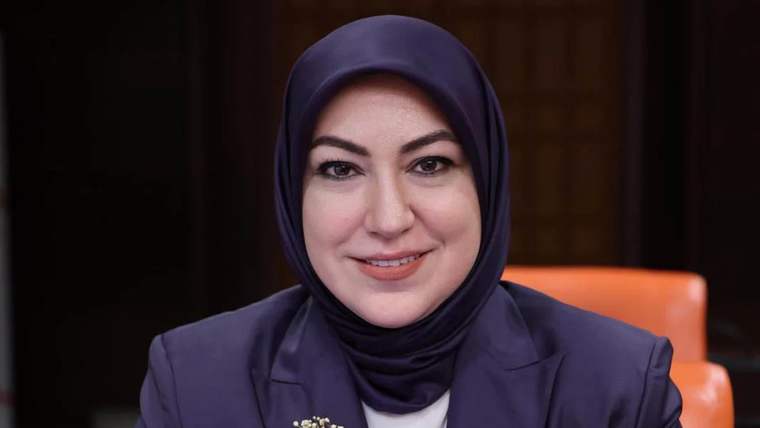 Başında başörtüsü olan bir kadın, gülümseyerek kameraya bakıyor.