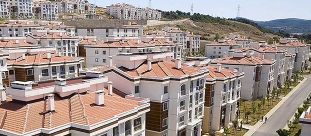 Kırmızı kiremit çatılı, çok katlı apartman blokları yamaçta ve birbirinin önünde sıralanıyor.