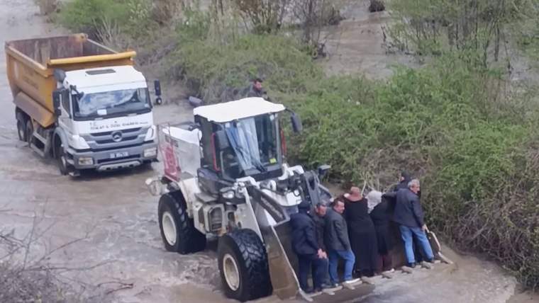 Sel sularında kepçeye binen insanlar, arka planda bir kamyon görünmekte.