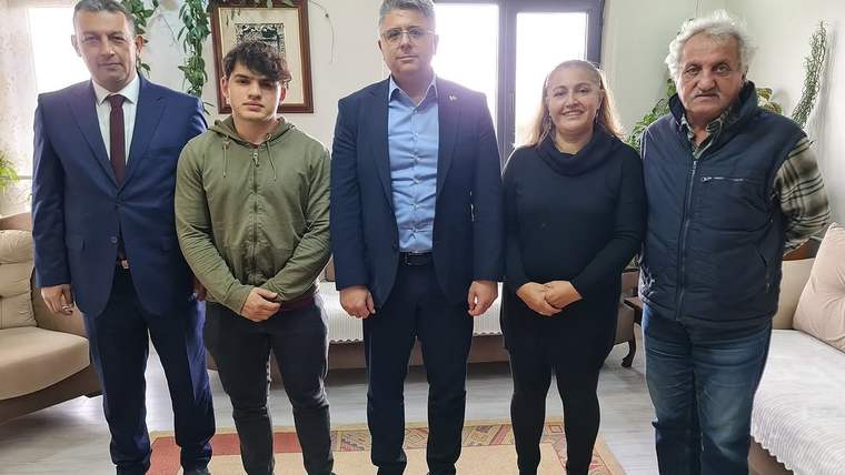 Beş kişi, bir odada yan yana duruyor; arka planda oturma grubu ve bitkiler var.
