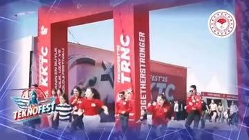 TEKNOFEST alanında kırmızı tişörtlü kişiler, üzerinde teknoloji ifadeleri bulunan stantların önünde duruyor.