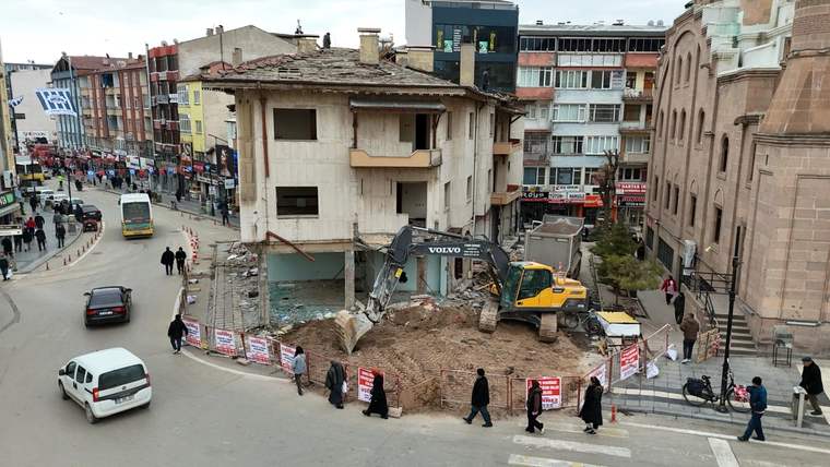 İş makinesi, çevresine güvenlik şeridi çekilen eski bir binanın yıkım alanında çalışıyor.