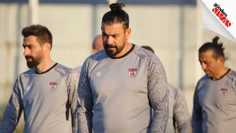 Antrenman kıyafetleri giymiş futbolcular, sahada yürüyüş yapıyor.