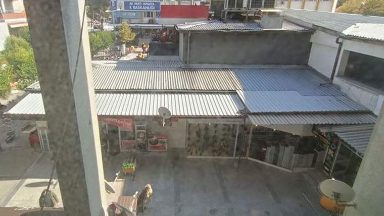 Isparta'da bir iş yerinin önünde boş bir alan, çevrede dükkanlar ve ağaçlar görünmekte.