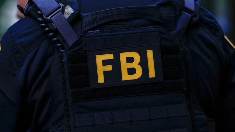 Siyah taktik yelek giyen kişinin göğsünde sarı harflerle FBI yazısı görülüyor.