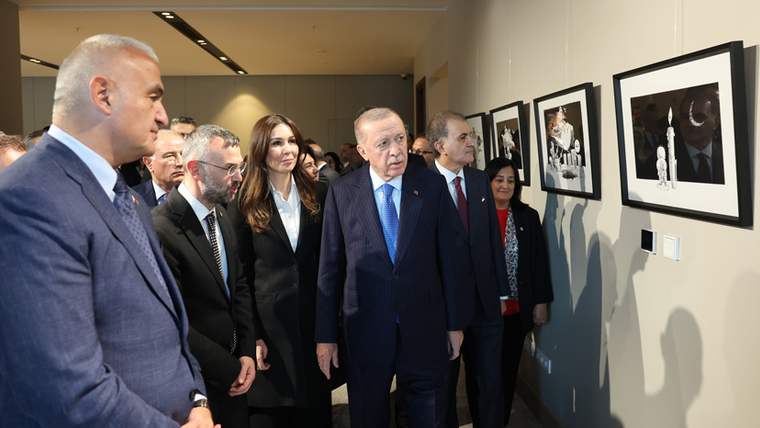 Cumhurbaşkanı Erdoğan ve yanındaki kişiler, duvarda asılı fotoğrafları inceliyor.