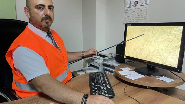 Turuncu yelek giymiş bir uzman, bilgisayar ekranında harita göstererek açıklama yapıyor.