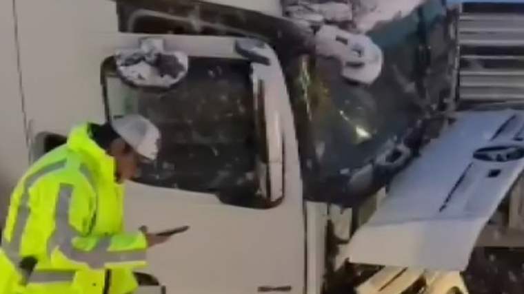 Beyaz bir kamyonun ön kısmı hasar görmüş, yanında sarı montlu bir kişi cep telefonuyla ilgileniyor.
