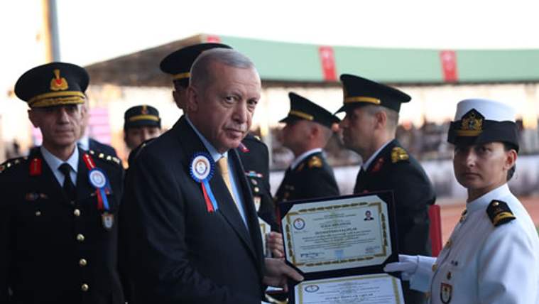 Takım elbiseli bir erkek, üniformalı kadın görevlinin uzattığı iki belgeyi alırken çevresinde görevliler duruyor.